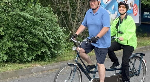 Petra Bognitz und ihr Pilot Volker Weinlich fahren auf einem Tandem eine Straße entlang. Beide tragen einen Helm.