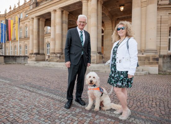 Vor dem Neuen Schloss in Stuttgart stehen von links nach rechts Ministerpräsident Winfried Kretschmann, Festivalführhund Harry und Sichtweisen-Redakteurin Lisa Mümmler.