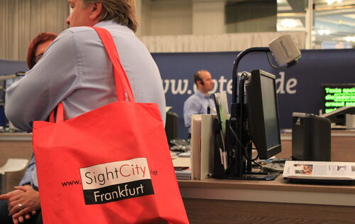 Ein Bild aus dem Messegeschehen. Im Vordergrund leuchtet eine rote Tasche, auf der "SightCity Frankfurt" steht.