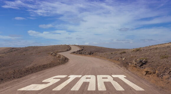 "Start" steht in großen Lettern auf einer Straße, die gewunden zum Horizont führt.