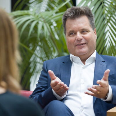Das Bild zeigt Jürgen Dusel im Gespräch mit einer anderen Person. Er trägt einen dunkelblauen Anzug und ein weißes Hemd