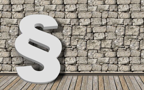 Ein weißer Paragraph vor einer groben, grauen Steinmauer.