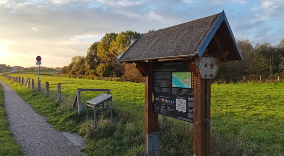 Am Wegesrand steht eine Infotafel zum Planeten Erde, daneben ist die entsprechende Station des Planetenlehrpfades in Wedel. Der Weg führt weiter in die Ferne, umgeben von Wiesen.