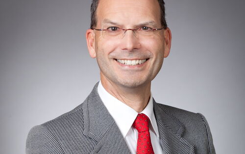 Stefan Insam lächelt in die Kamera. Er hat kurzes Haar, und trägt eine kleine randlose Brille. Unter einem Sakko trägt er ein weißes Hemd und eine Krawatte.