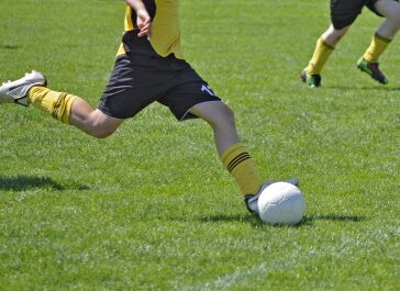 Jemand schießt schwungvoll einen weißen Fußball. Das Trikot ist gelb und schwarz.