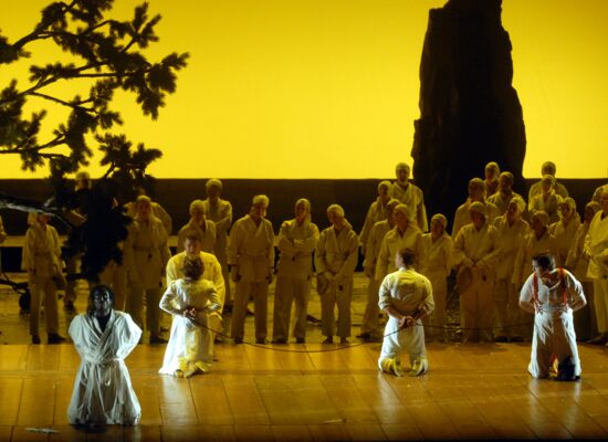 AudioSzene aus der „Zauberflöte“ an der Deutschen Oper Berlin: Viele Menschen sind zu sehen, im Vordergrund knien vier Gefangene.