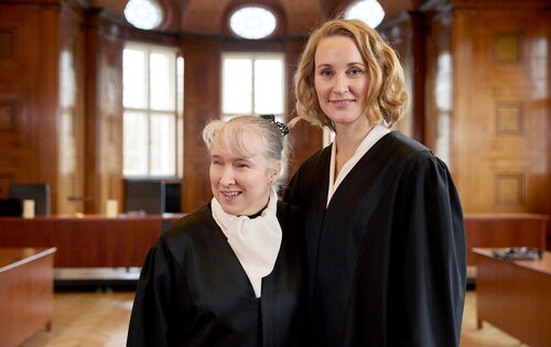 Pamela Pabst und Christina Athenstädt, beide in schwarzer Robe, stehen in einem  Gerichtssaal, Pamela Pabst trägt ihr helles Haar hochgesteckt.