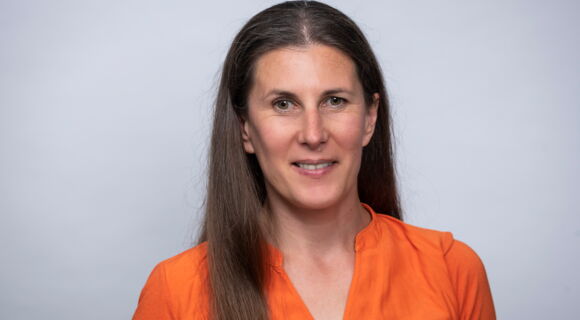 Ein Porträt von Rose Jokic: Sie lächelt in die Kamera. Ihr dunkles, langes Haar hat sie über eine Schulter gelegt. Sie trägt eine Bluse.