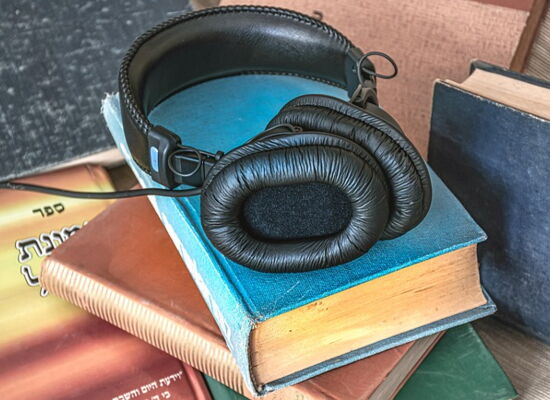 Ein schwarzer Kopfhörer mit gepolsterten Ohrmuscheln liegt auf einem Stapel Bücher. Auch daneben stehen Bücher.