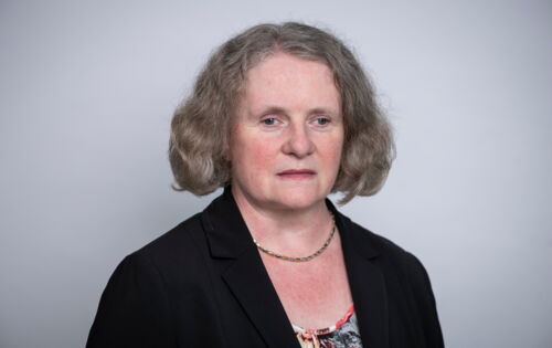 Silvia Hame hat halblange, graue Haare. Sie trägt einen dunklen Blazer über einem blumigen Oberteil.