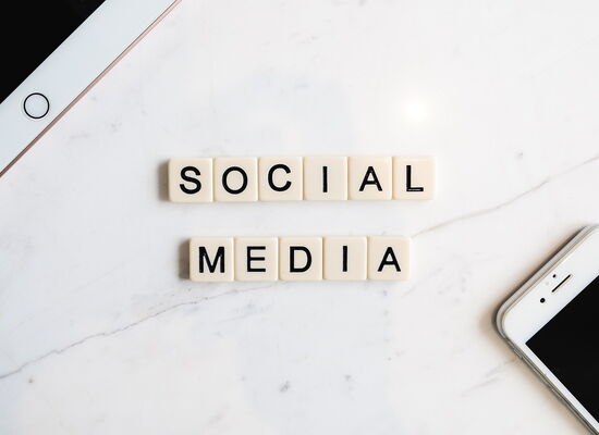 Der Begriff "Social Media" wurde aus Scrubble-Steinen gelegt. Daneben liegen Tablet und Smartphone.