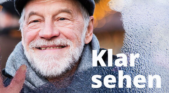 Ein älterer Mann mit grauem Bart und Mütze blickt lächelnd durch eine beschlagene Glasscheibe. Die rechte Hand wischt das Glas frei. Rechts unten steht in weißer Schrift „Klar sehen“.
