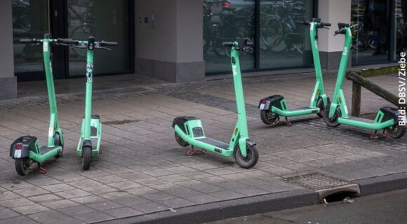 Fünf grüne E-Roller stehen kreuz und quer auf dem Gehweg.