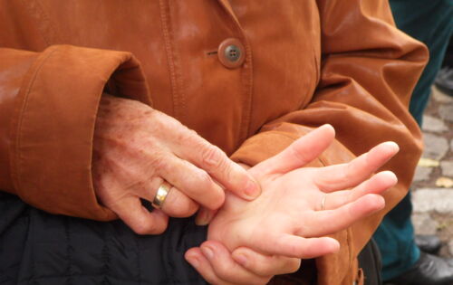 Nahaufnahme von sich berührenden Händen beim Lormen: Die linke Hand einer Person liegt mit der Handfläche nach oben in der linken Hand einer zweiten Person. Diese tippt mit den Fingern ihrer rechten Hand Lormzeichen in die Hand der ersten Person.