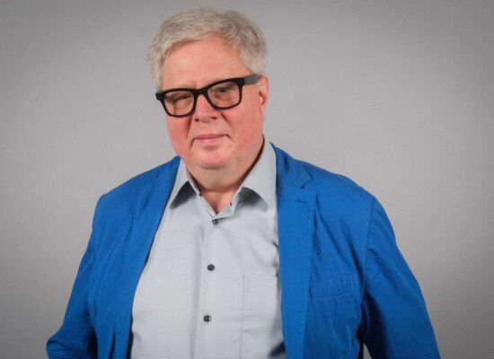 Porträt von Thomas Kahlisch. Er hat kurzes, weißgraues Haar und trägt eine dunkle Brille. Über ein hellblaues Hemd hat er ein Sakko in mittlerem Blau gezogen.