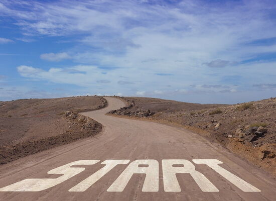 "Start" steht in großen Lettern auf einer Straße, die gewunden zum Horizont führt.