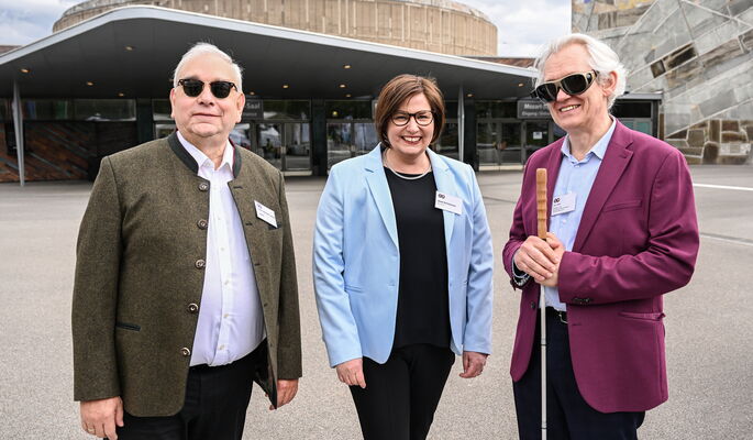Vor der Liederhalle stehen lächelnd v.l.n.r. Hans-Werner Lange, Präsident Deutscher Blinden- und Sehbehindertenverband, Anne Reichmann, Vorstandsvorsitzende Nikolauspflege und Arne Jöns, Vorsitzender Blinden- und Sehbehindertenverband Württemberg.