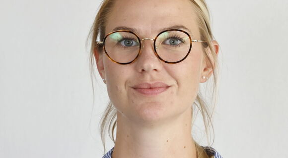 Melissa Glomb hat ihr blondes, glattes Haar zusammengebunden und trägt eine Brille mit runden Brillengläsern und eine helle Hemdbluse.