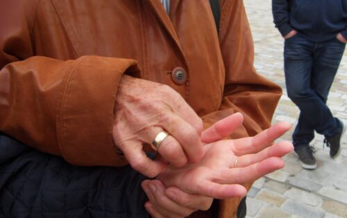 Eine Frau mit braunem Ledermantel lormt auf der Hand eines anderen Menschen. An ihrem Ringfinger ist ein breiter, goldener Ring.