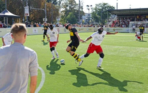 Szene aus einem Blindenfußballspiel: Drei Spieler, davon zwei aus einer Mannschaft, kämpfen um den Ball.
