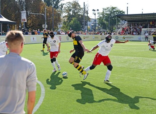 Szene aus einem Blindenfußballspiel: Drei Spieler, davon zwei aus einer Mannschaft, kämpfen um den Ball.