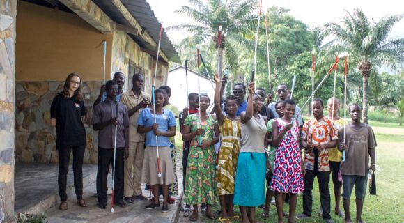 Ein Gruppenbild zeigt togolesische Schülerinnen und Schüler, die Langstöcke erhalten haben und sie nach oben in die Luft halten. Jasmin Ciplak steht links am Rand der Gruppe.