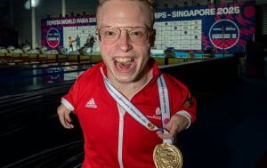 Josia Topf freut sich über seine Goldmedaille. Er ist ein bonder Mann mit TAR-Syndrom, und hat sehr kurze Arme. Er hat den Mund freudig geöffnet und strahlt in die Kamera.