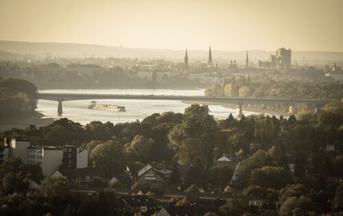 Blick in die Ferne auf die Silhouette von Bonn. Eine lange Brücke spannt sich in der Mitte des Bildes über den Rhein.