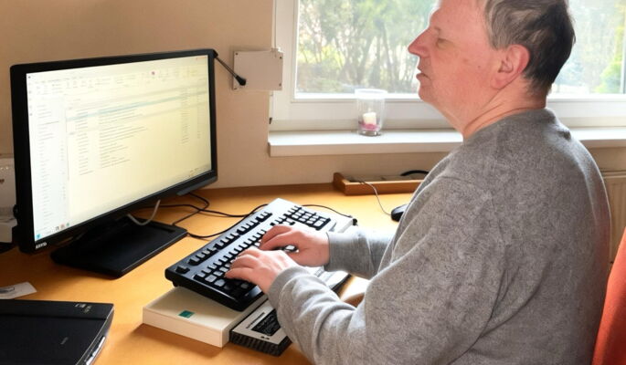 Bruno Etzenberger sitzt an einem Fensterplatz am Computer. Er hat kurze helle Haare und trägt einen grauen Pullover.