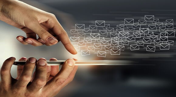 Eine Hand hält ein Smartphone, eine andere tippt auf das Display. Zahllose E-Mail-Symbole fliegen heraus.