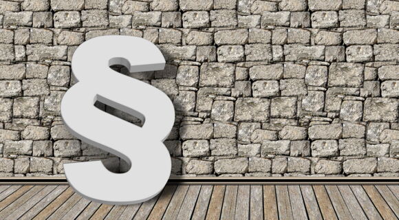 Ein weißer Paragraph vor einer groben, grauen Steinmauer.