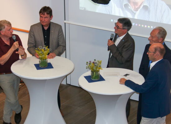 Oded Heilbronner, Andreas Bethke und Hans Neugebauer stehen bei der Gesprächsrunde an weißen Tischen. Prof. Heilbronner hält ein Mikrofon.