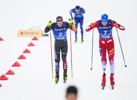 Para-Skilangläufer Sebastian Marburger fährt auf einer beschneiten Piste neben einem anderen Sportler. Beide tragen enge Skianzüge und stoßen mit den Skistöcken in den Schnee.