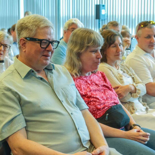 Prof. Thomas Kahlisch und Andrea Katemann sitzen nebeneinander im Plenum. Um sie herum andere Teilnehmende des DBSV-Verbandstags. Ihre Aufmerksamkeit ist auf den vorderen Teil des Seminarraums gerichtet.