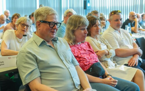 Prof. Thomas Kahlisch und Andrea Katemann sitzen nebeneinander im Plenum. Um sie herum andere Teilnehmende des DBSV-Verbandstags. Ihre Aufmerksamkeit ist auf den vorderen Teil des Seminarraums gerichtet.