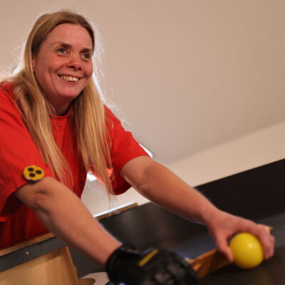 Mandy Kugel hat langes, helles Haar und trägt ein rotes Shirt. Sie beugt sich lächelnd über einen Showdown-Tisch, in der linken Hand hält sie einen Ball.