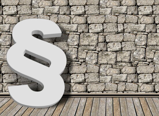 Ein weißer Paragraph vor einer groben, grauen Steinmauer.