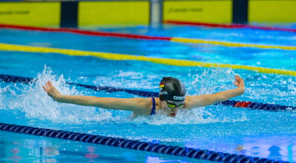Die 14-jährige Johanna Döhler schwimmt in Schmetterlingstechnik, auch Delfin genannt, eine Bahn: Sie hat die Arme zur Seite ausgebreitet und holt Luft. Sie trägt eine dunkle Badekappe und eine Schwimmbrille.
