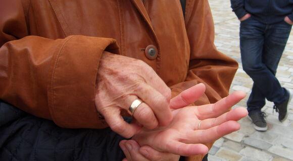 Eine Frau mit braunem Ledermantel lormt auf der Hand eines anderen Menschen. An ihrem Ringfinger ist ein breiter, goldener Ring.