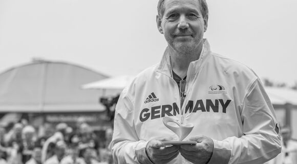 Dr. Karl Quade mit einer Trophäe bei den Paralympics in Rio de Janeiro. Er trägt kurzes, schütteres Haar und hat einen Dreitagebart. Er lächelt in die Kamera. Auf seiner hellen Jacke steht „GERMANY“.