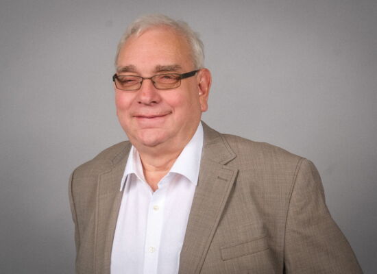 Porträt von Hans-Werner Lange. Er trägt ein weißes Hemd, ein hellbeiges Sakko und eine dunkle Brille. Sein kurzes, weißes Haar ist sorgfältig gekämmt. Er lächelt leicht in die Kamera..