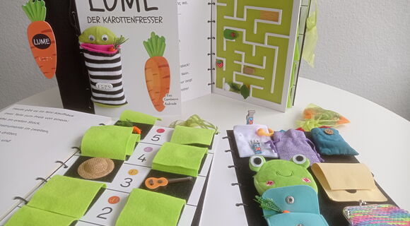 Interaktives Tastbuch „Lume der Karottenfresser“ mit Stofffiguren, Taschen, Labyrinth und verschiedenen taktilen Spielelementen auf mehreren geöffneten Buchseiten.