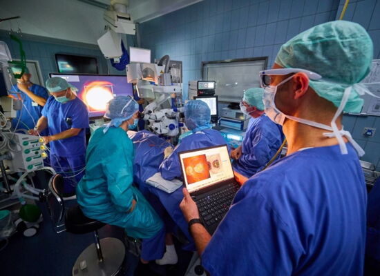 Implantation - eines elektronischen Netzhaut-Chips in der Augenklinik des UKB durch Prof. Frank Holz. Mehrere Ärzte nehmen die OP vor und verfolgen sie über Bildschirme.