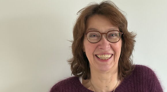 Anne Niesen lacht in die Kamera. Sie hat mittellange, wellige, dunklere Haare und trägt eine Brille mit dunklem Rahmen.