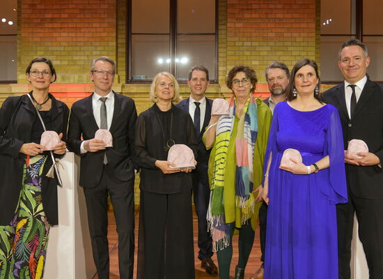 In festlicher Kleidung steht das AD-Team der Naturdokumentation „Unsere Meere“ auf der Bühne. Es gewann die ADele in der Kategorie „Dokumentation“.  Einige Team-Mtglieder halten die Keramik-Trophäe in den Händen.