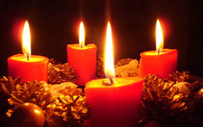 Vier rote Kerzen brennen auf einem Adventskranz. Er ist mit Tannenzapfen verziert. Die Kerzen schaffen ein warmes Licht.