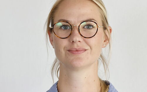 Melissa Glomb hat ihr blondes, glattes Haar zusammengebunden und trägt eine Brille mit runden Brillengläsern und eine helle Hemdbluse.