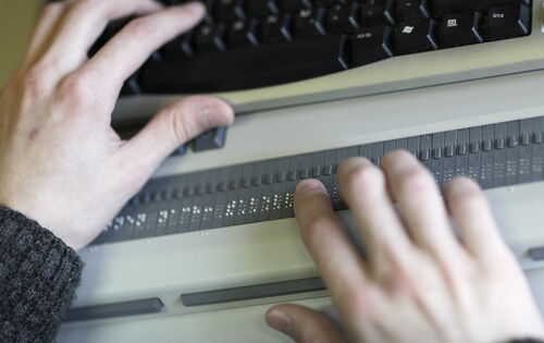 Ein Paar Hände liest auf einer Braillezeile an einem Laptop.
