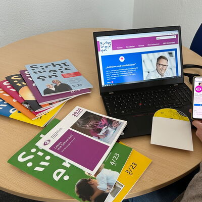 Auf einem Tisch steht ein Laptop, das eine Seite von Sichtweisen-online zeigt. Daneben ein Stapel Sichtweisen-Hefte, die Publikation „Weitersehen 2024“ und eine Daisy-CD.
