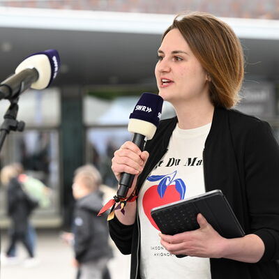 Tomke Koop beschreibt das Geschehen auf dem Berliner Platz und macht es so für blinde und sehbehinderte Festivalgäste sichtbar. Sie hält ein Mikrofon und ein Tablet in der Hand.